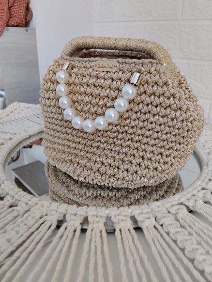 detail-anses-perles-blanches-sac-madame-crochet Gros plan détaillé sur les perles blanches délicates formant les anses du sac de cérémonie doré Madame Crochet. حقيبة يد ذهبية للمناسبات والأعراس (Sac à main doré pour événements et mariages) حقيبة كروشيه يدوية الصنع خيط ذهبي (Sac en crochet fait main fil doré) صناعة تقليدية تونسية فاخرة مدام كروشيه (Artisanat traditionnel tunisien de luxe Madame Crochet) حقيبة يد نسائية راقية بالخرز الأبيض (Sac à main pour femme raffiné avec perles blanches)